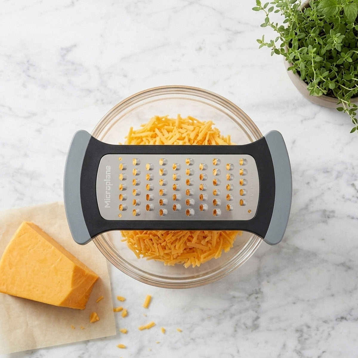 Handheld grater with shredded cheese in a glass bowl on a marble surface