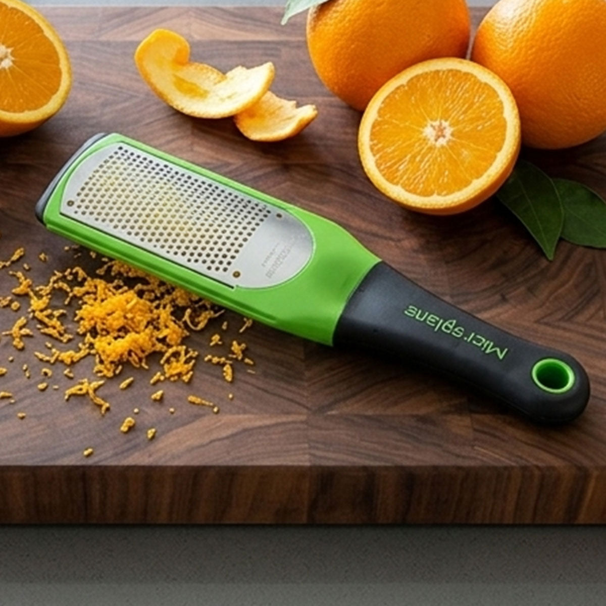 Green microplane grater with orange zest on a wooden surface with oranges