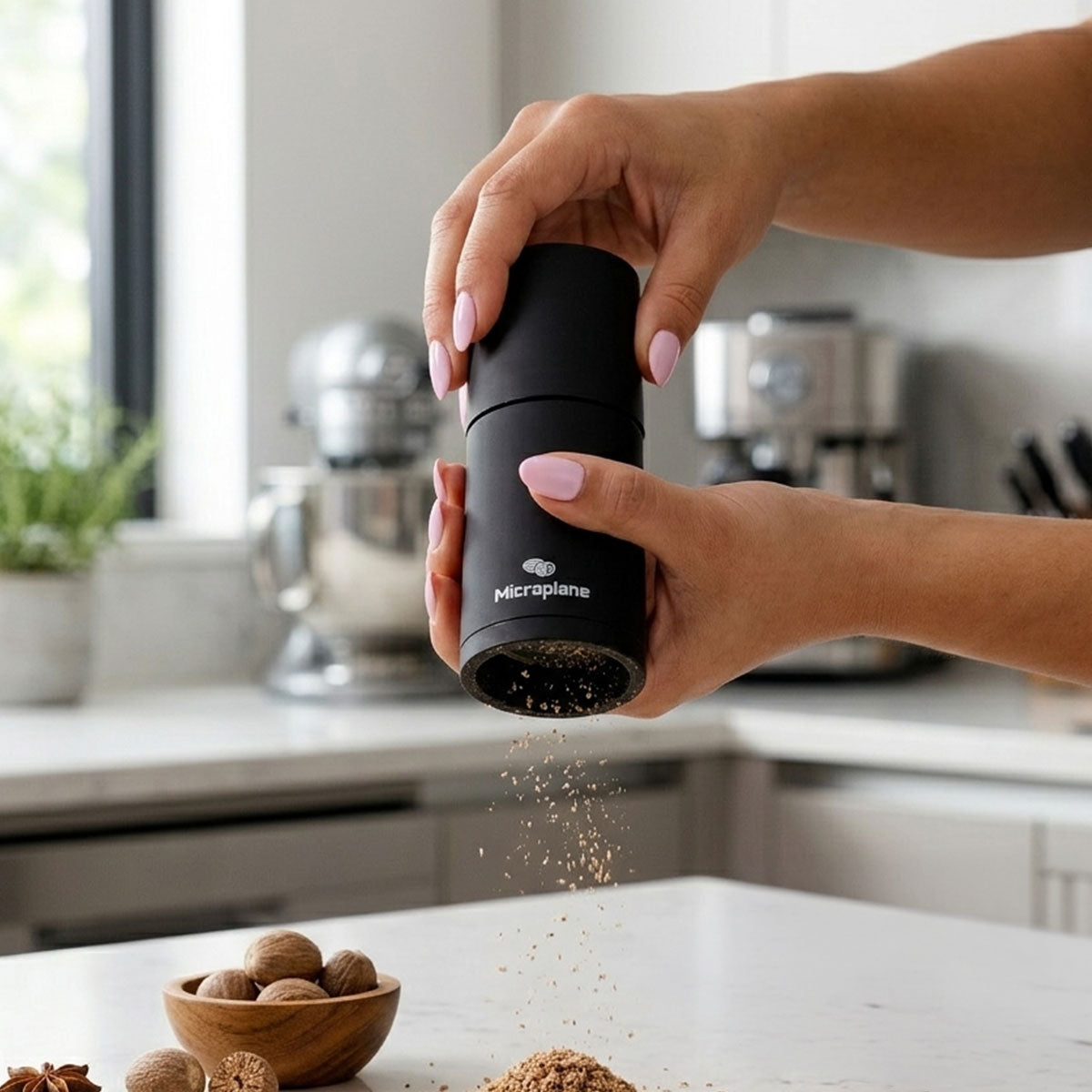 Person using a black Microplane pepper grinder in a kitchen setting