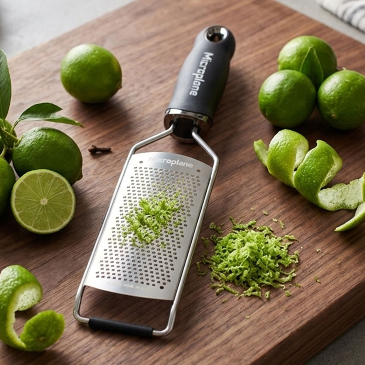 Microplane zester on a wooden cutting board with limes and lime zest