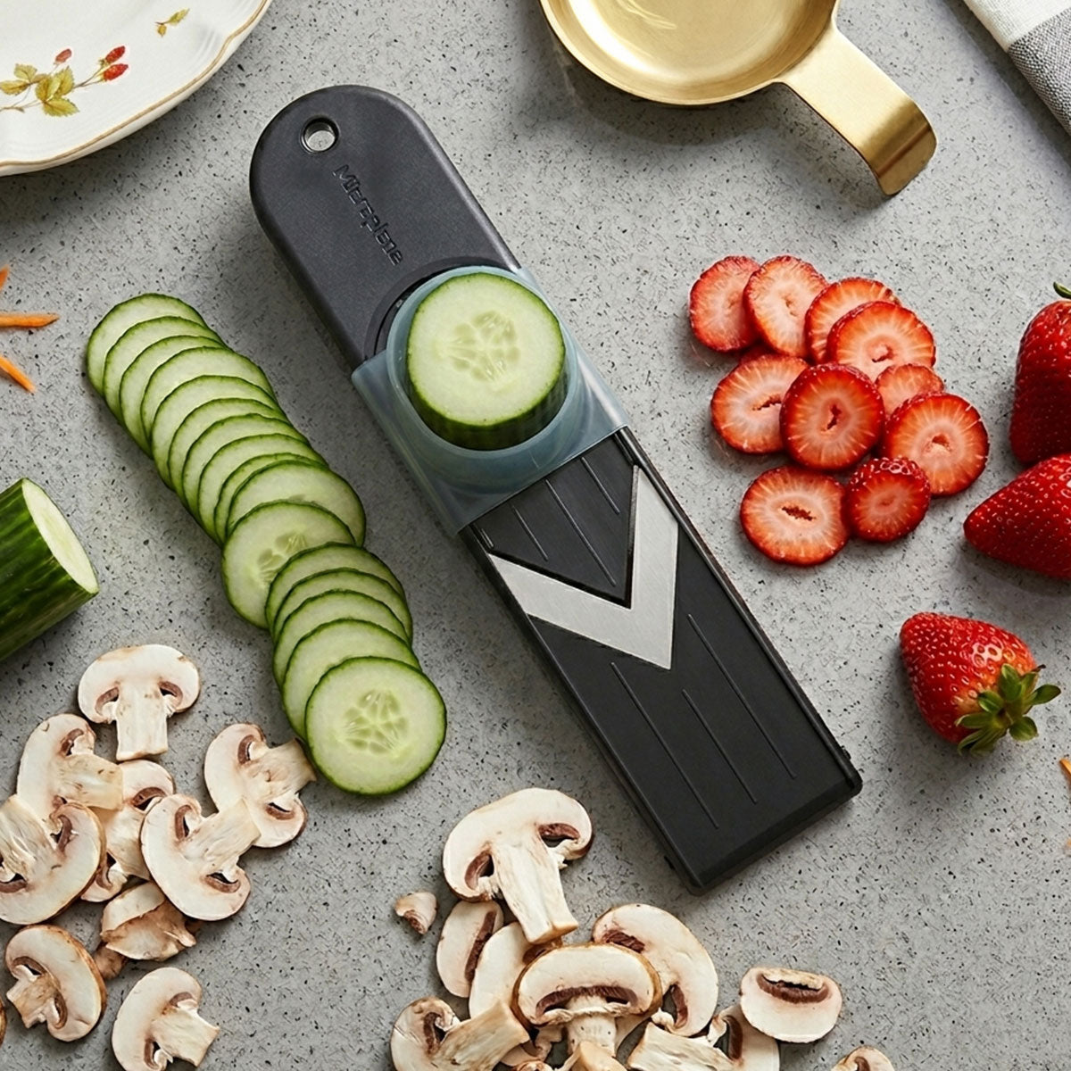 Vegetable peeler with sliced cucumbers, strawberries, and mushrooms on a gray surface
