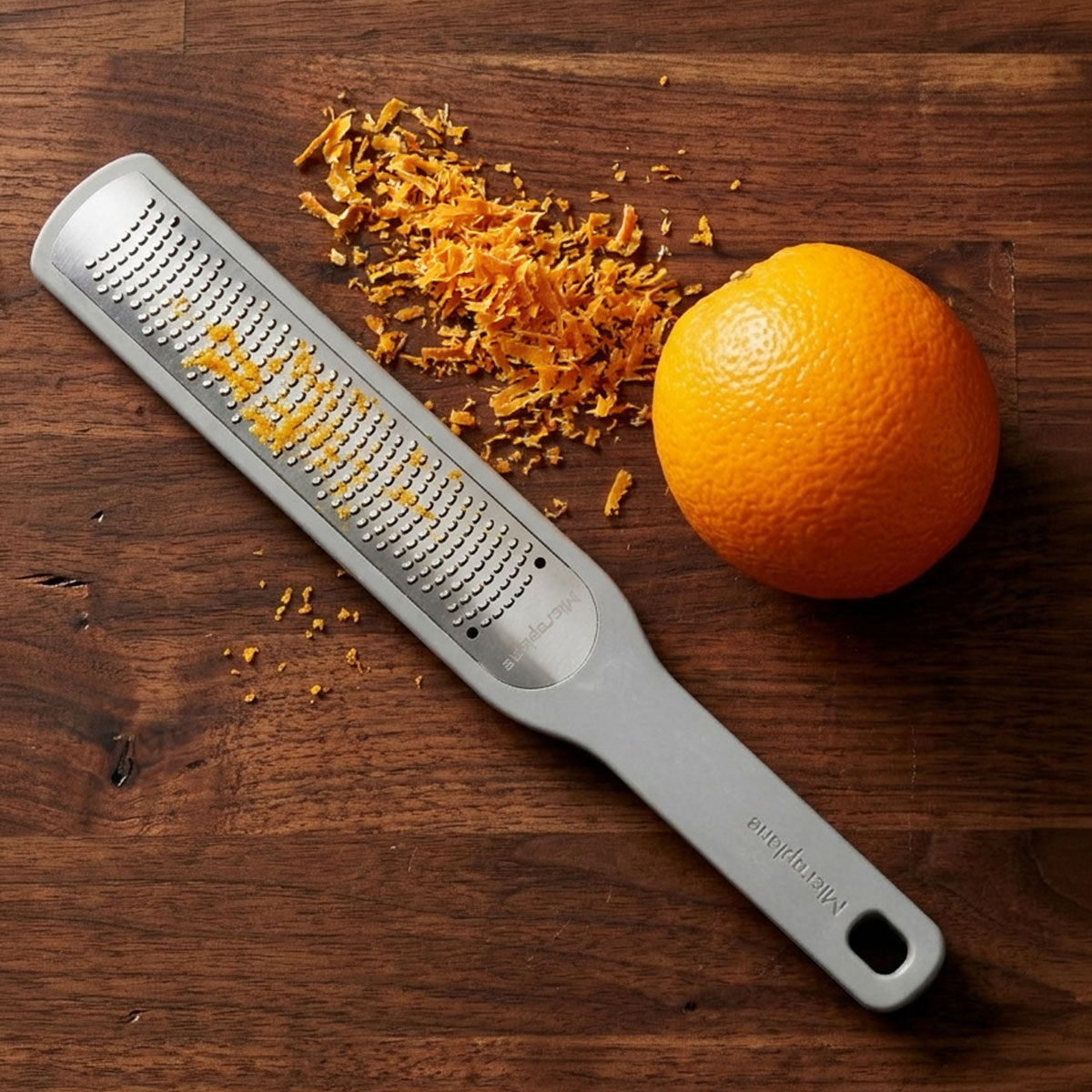 Zester with orange zest and an orange on a wooden surface