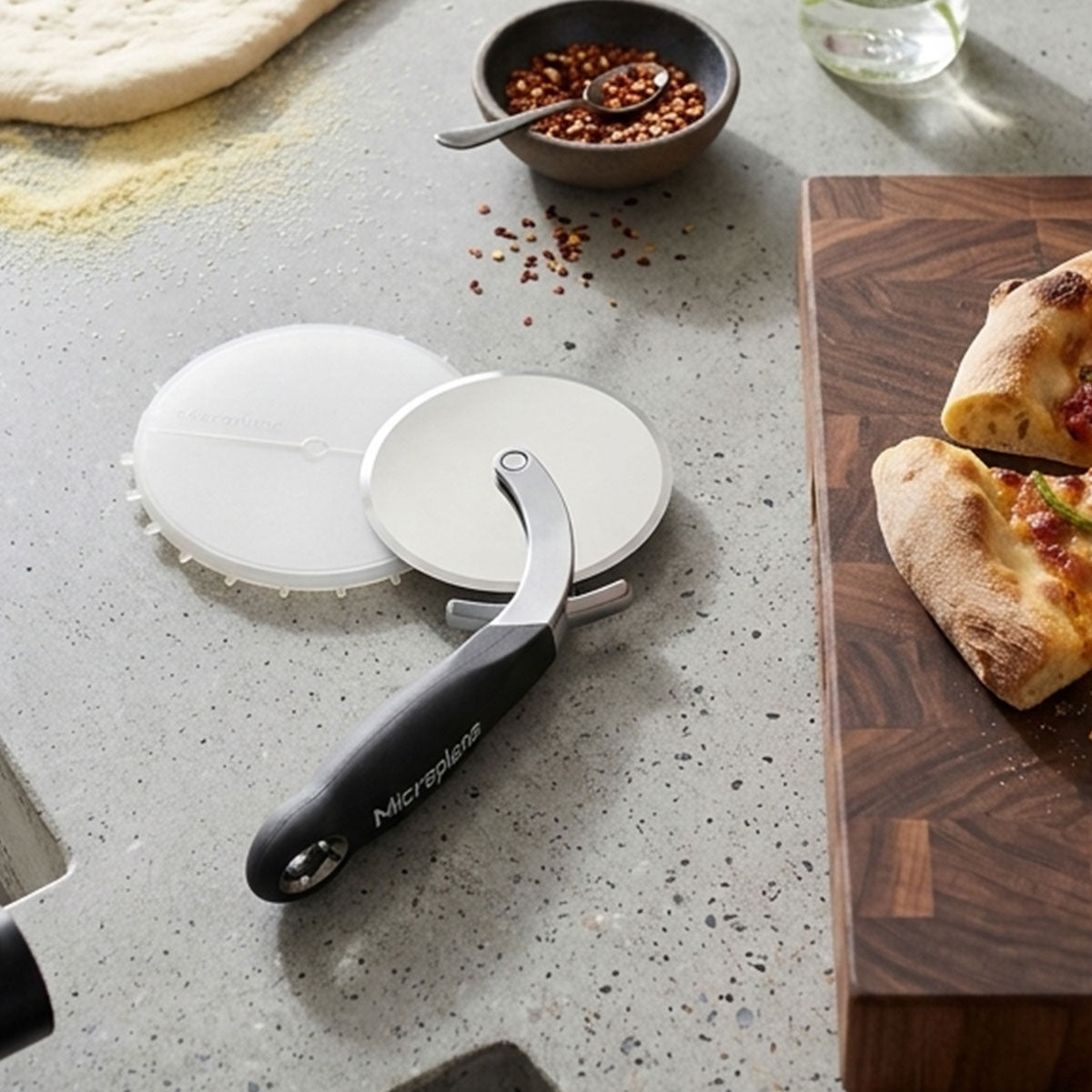 Pizza cutter on a kitchen counter with pizza and ingredients