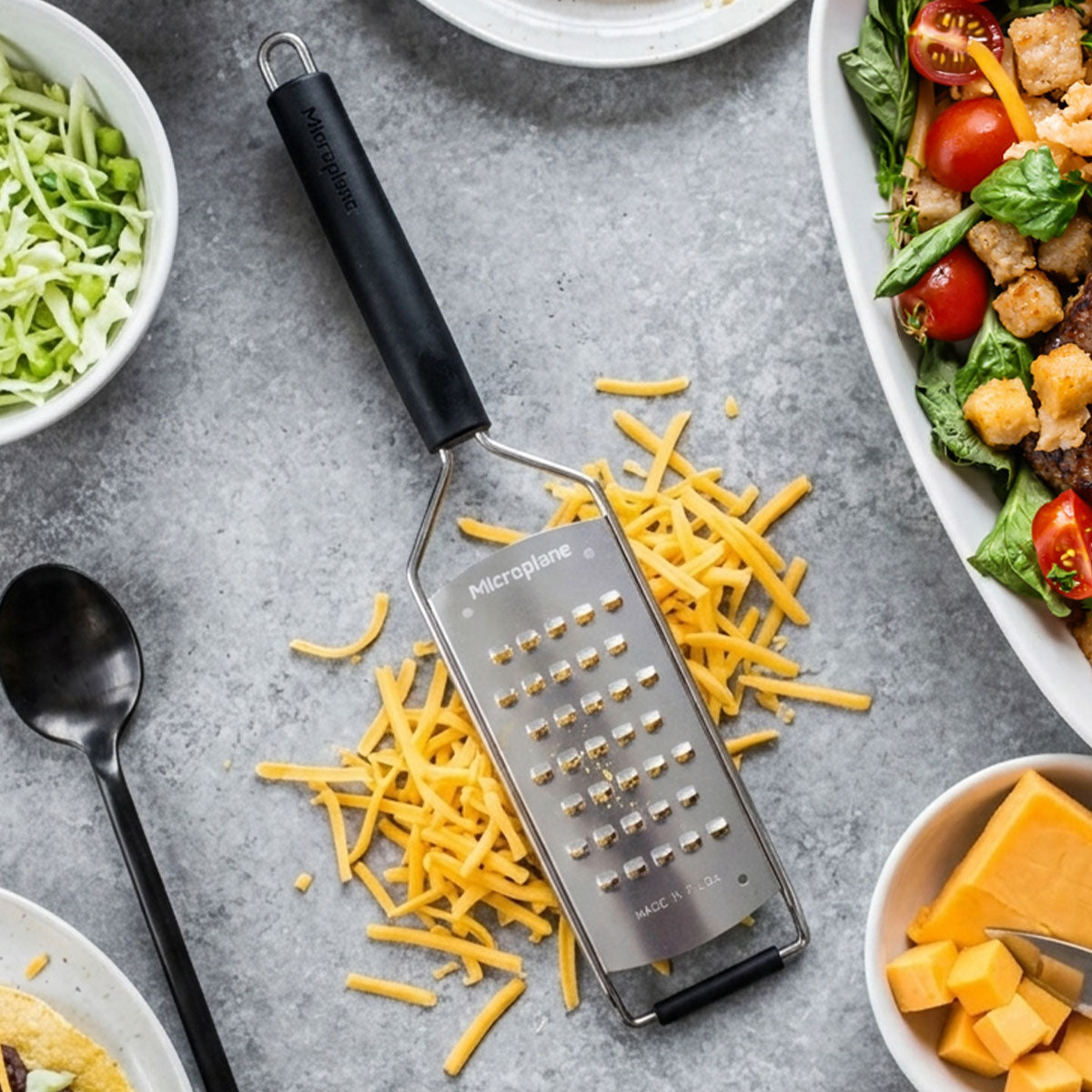 Microplane grater with shredded cheese on a gray surface with food items around