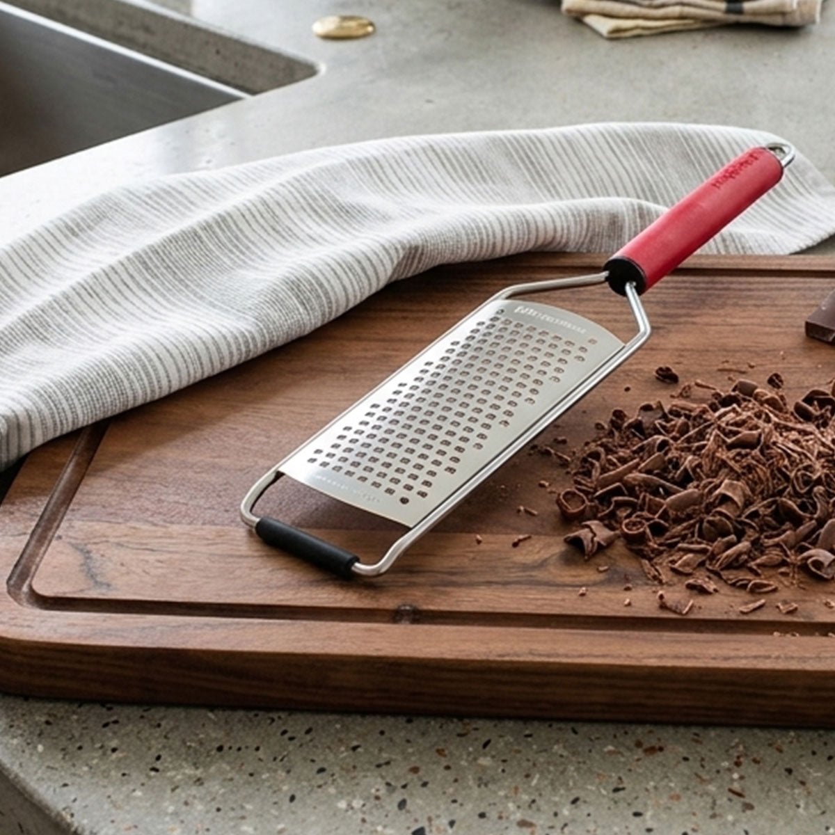Metal grater with red handle on a wooden cutting board next to grated chocolate