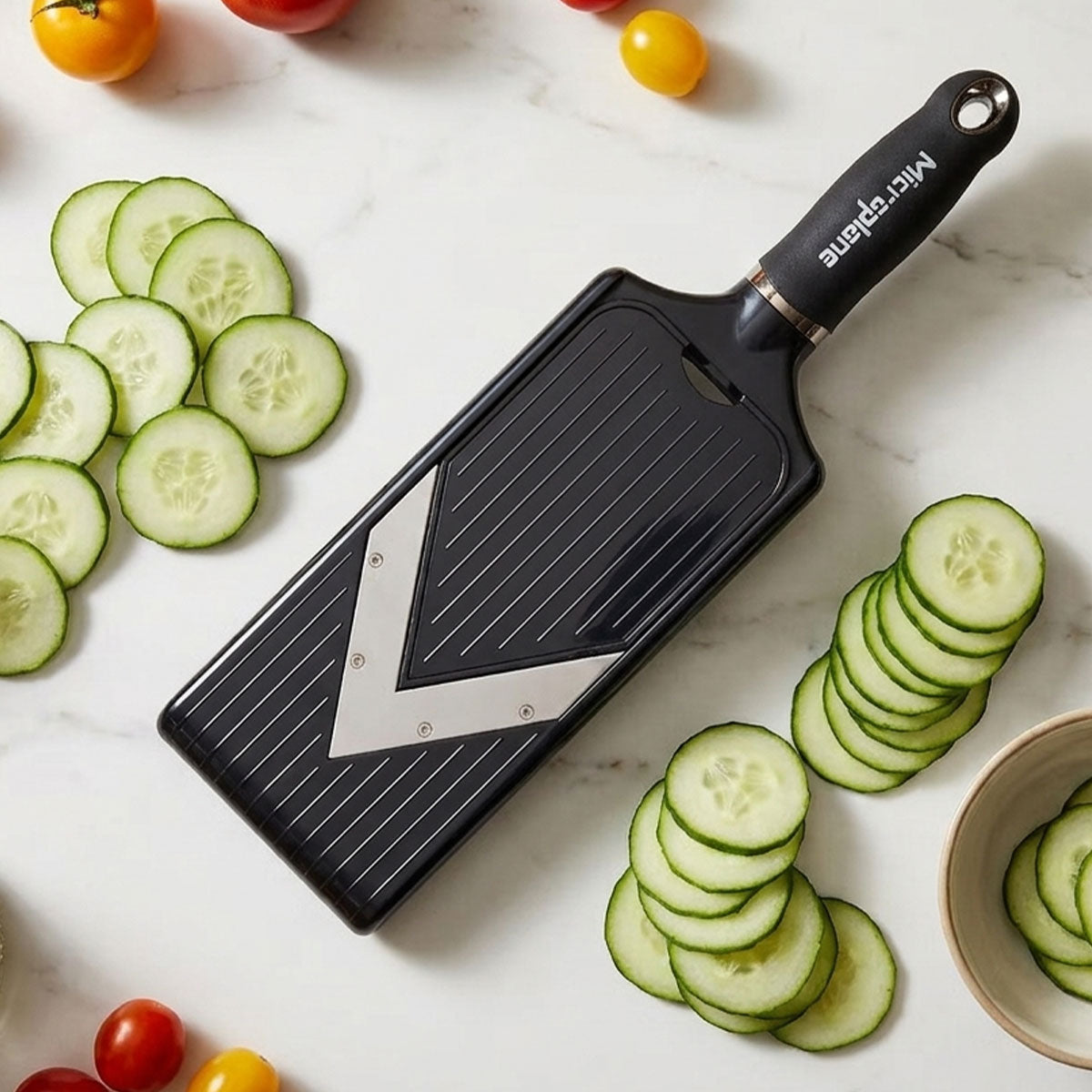 Black vegetable peeler with sliced cucumbers on a marble surface