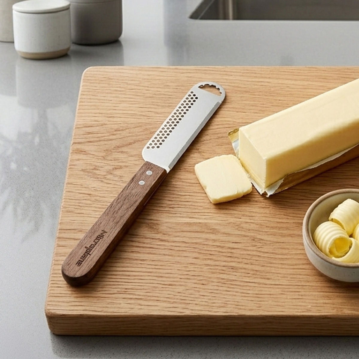 Butter knife and sliced butter on a wooden cutting board with a bowl of butter curls.